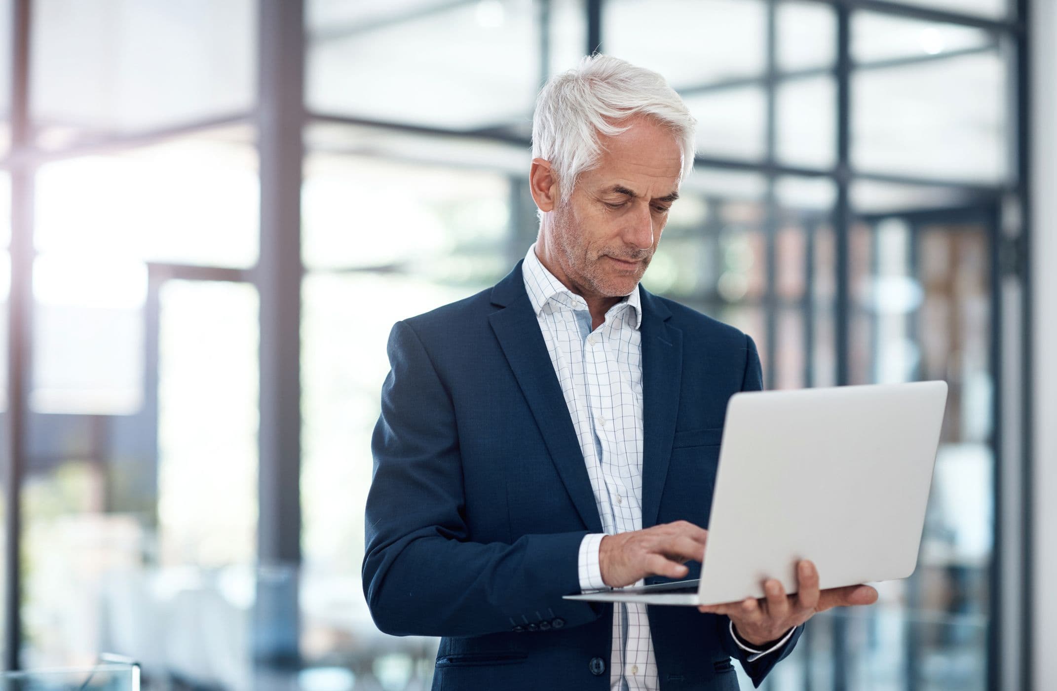 A grey-haired man in a suit jacket typing on a laptop.
