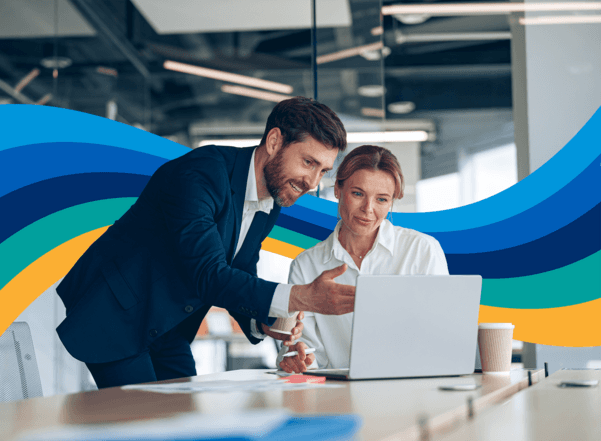 A man and woman collaborating, looking at a laptop in an office.