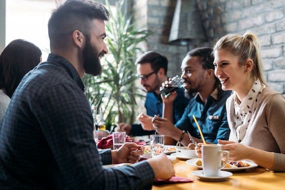 Diverse group of people smiling and eating in a restaurant.