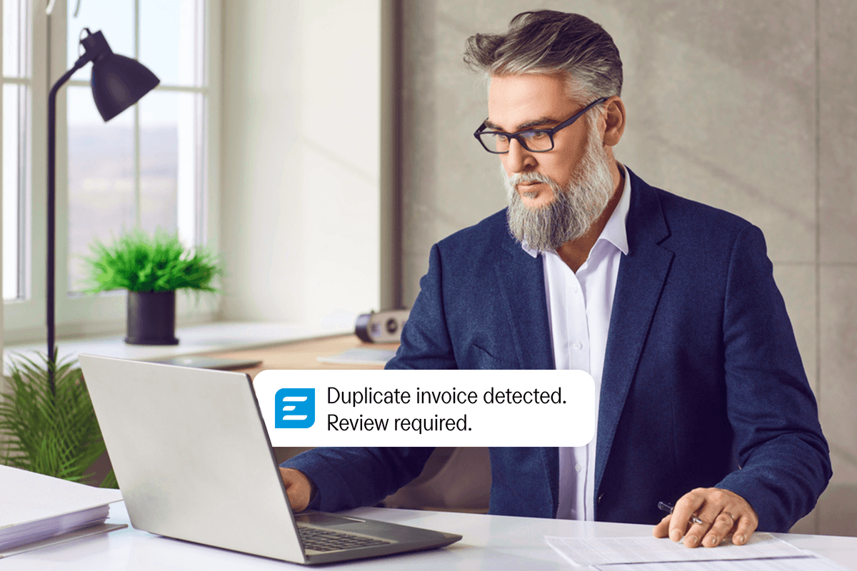 A man at a laptop sees a notification: "Duplicate invoice detected. Review required."