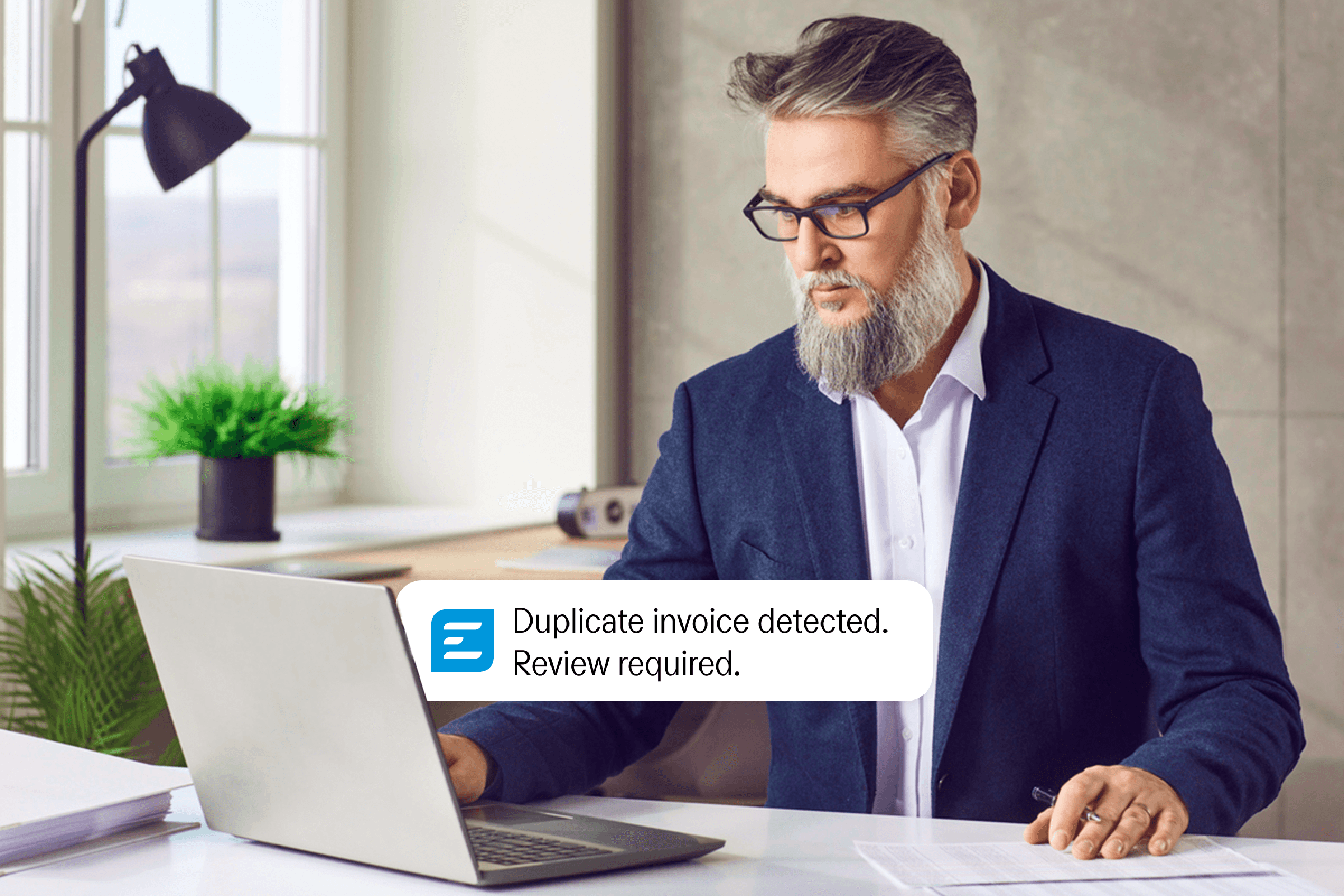 A man at a laptop sees a notification: "Duplicate invoice detected. Review required."