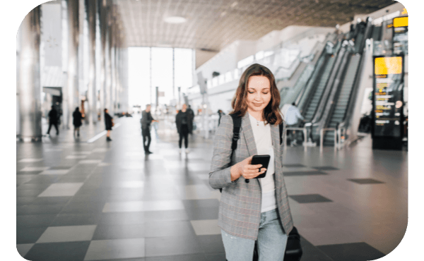Woman looking at her phone while walking through an airport with luggage.