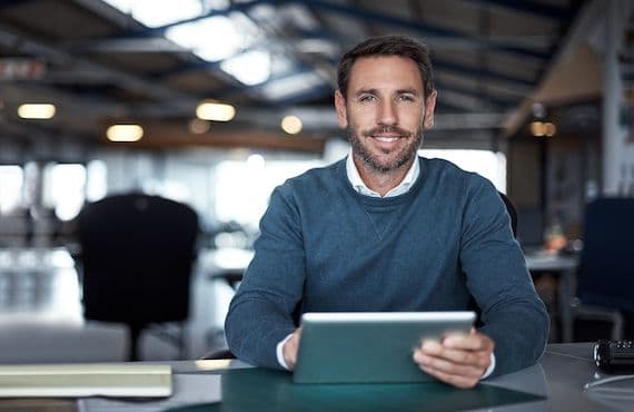 Smiling man in a blue sweater holding a tablet.