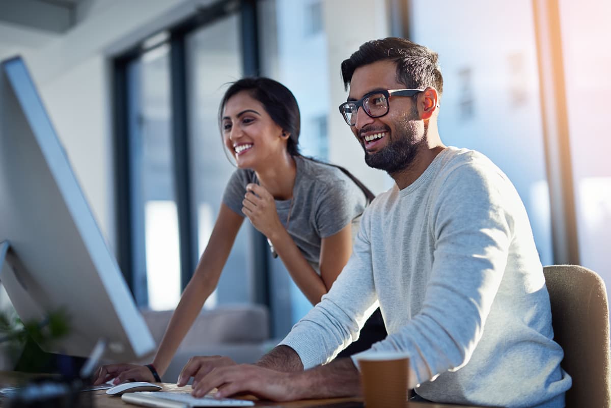 A man and woman smile while looking at a desktop computer screen.