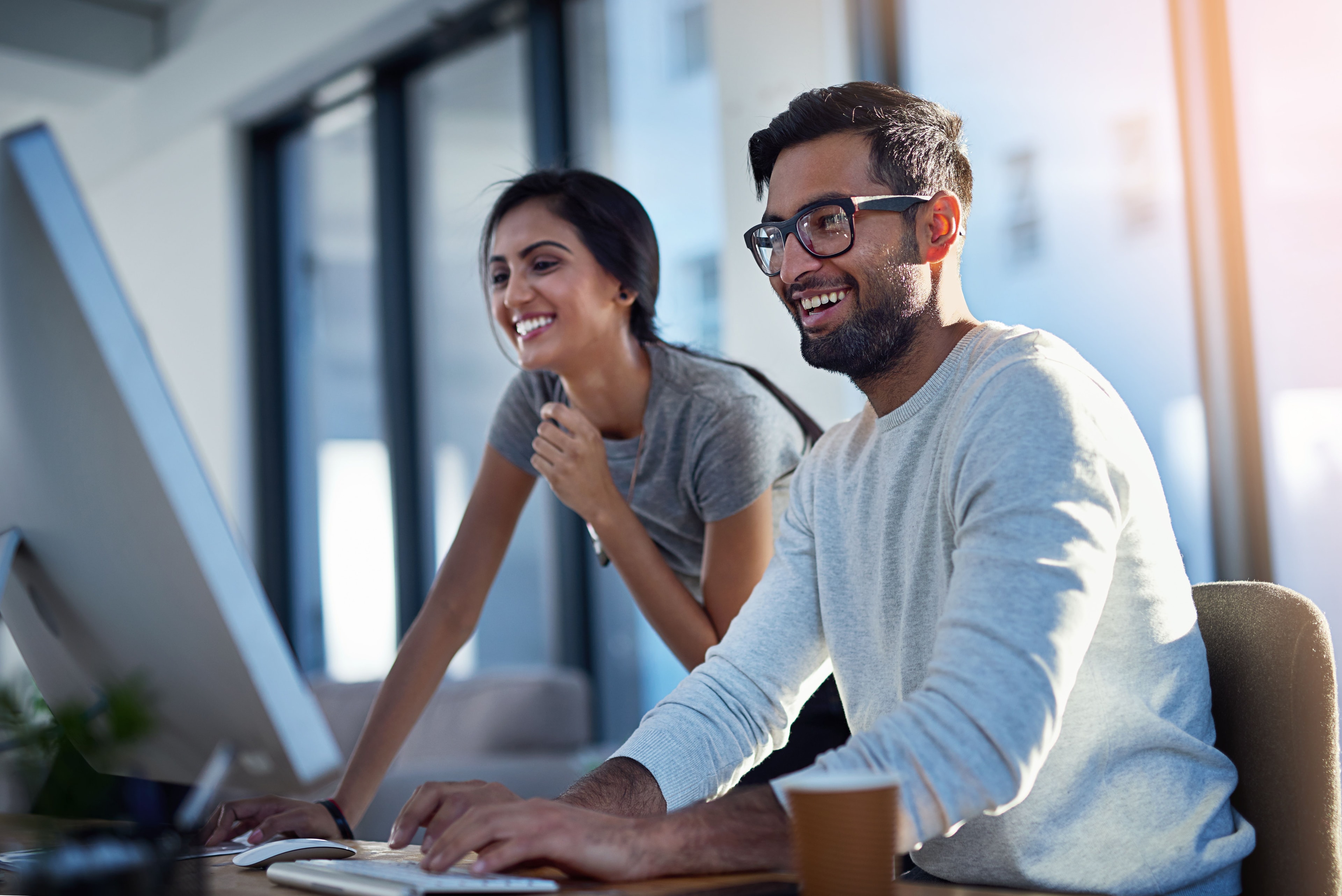 A man and woman smile while looking at a desktop computer screen.