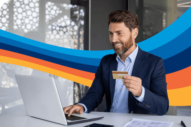 a man in a suit is holding a credit card in front of a laptop