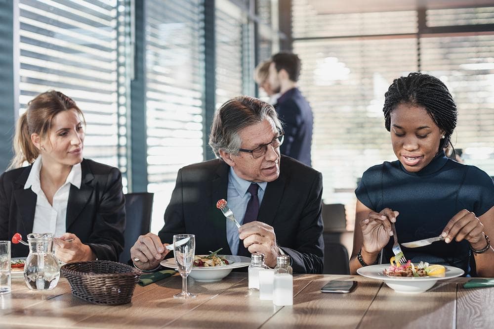 Three business colleagues eating lunch and conversing at a table.