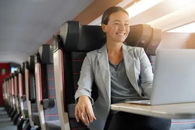 Smiling woman using a laptop on a train.