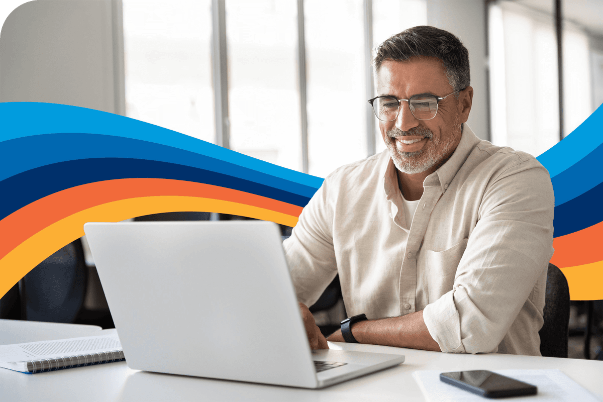Smiling man with glasses working on a laptop.