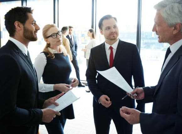 Four business people in suits discussing documents.
