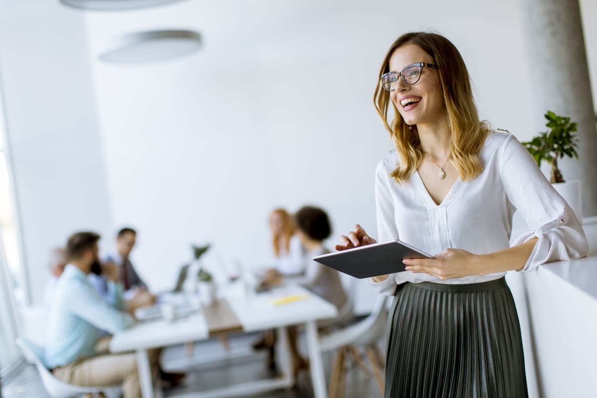 a woman is standing in an office holding a tablet and smiling .