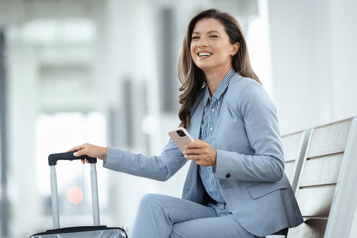 a woman in a suit sits with a suitcase and a cell phone