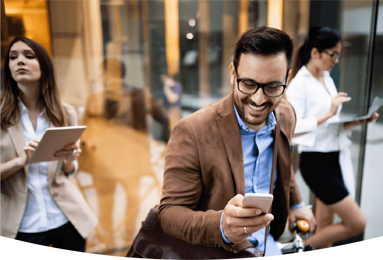 Smiling man using phone with two women using devices in the background.