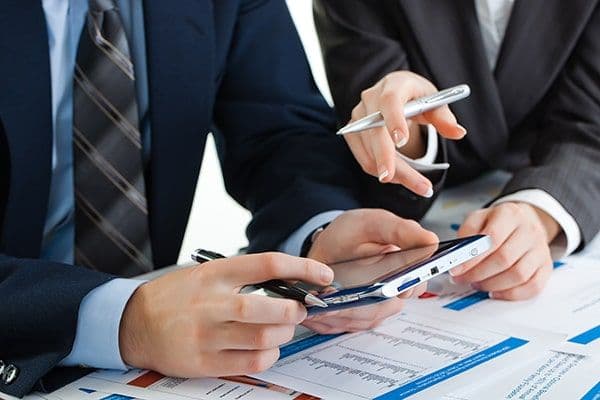 Duas pessoas de negócios a analisar dados num smartphone com documentos e gráficos.