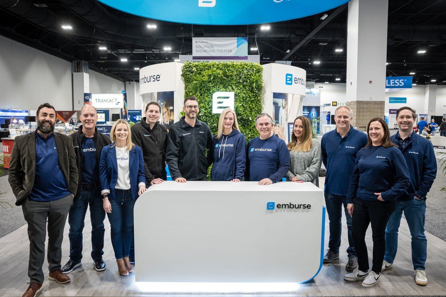 Eleven Emburse employees stand behind a branded counter at a trade show booth.