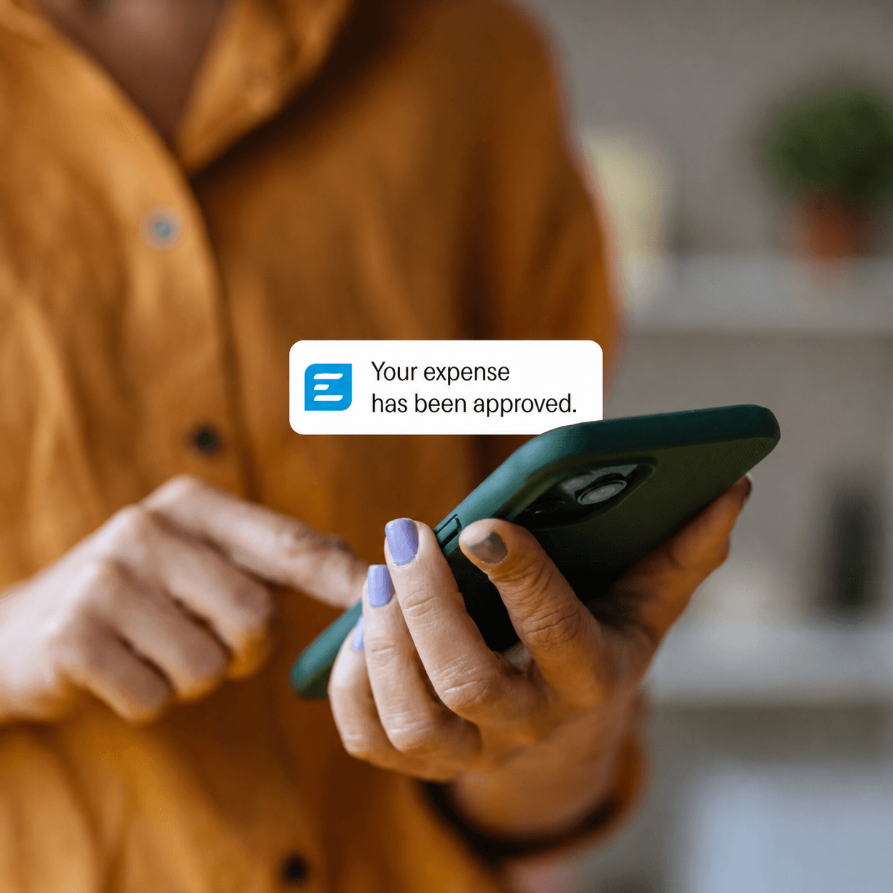 A person holding a smartphone receives a notification that reads, "Your expense has been approved."