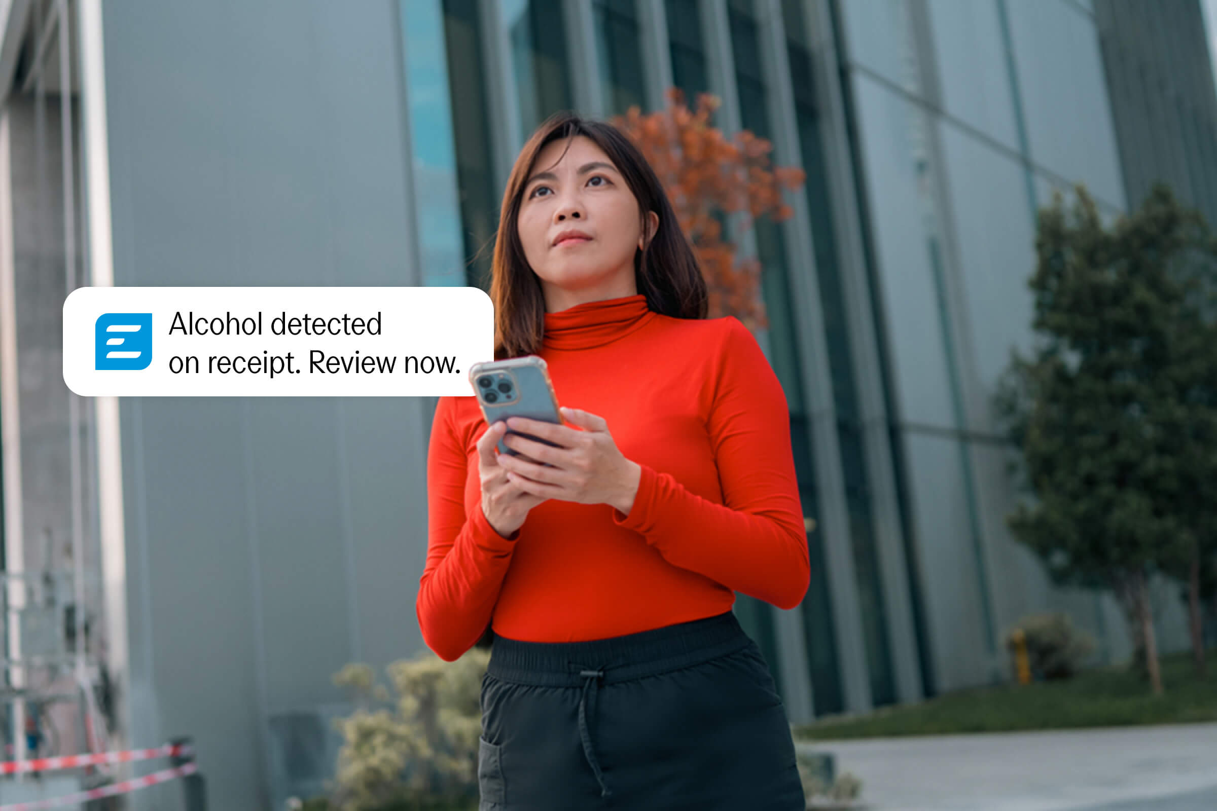 A woman holds a smartphone, with a notification bubble reading "Alcohol detected on receipt. Review now."