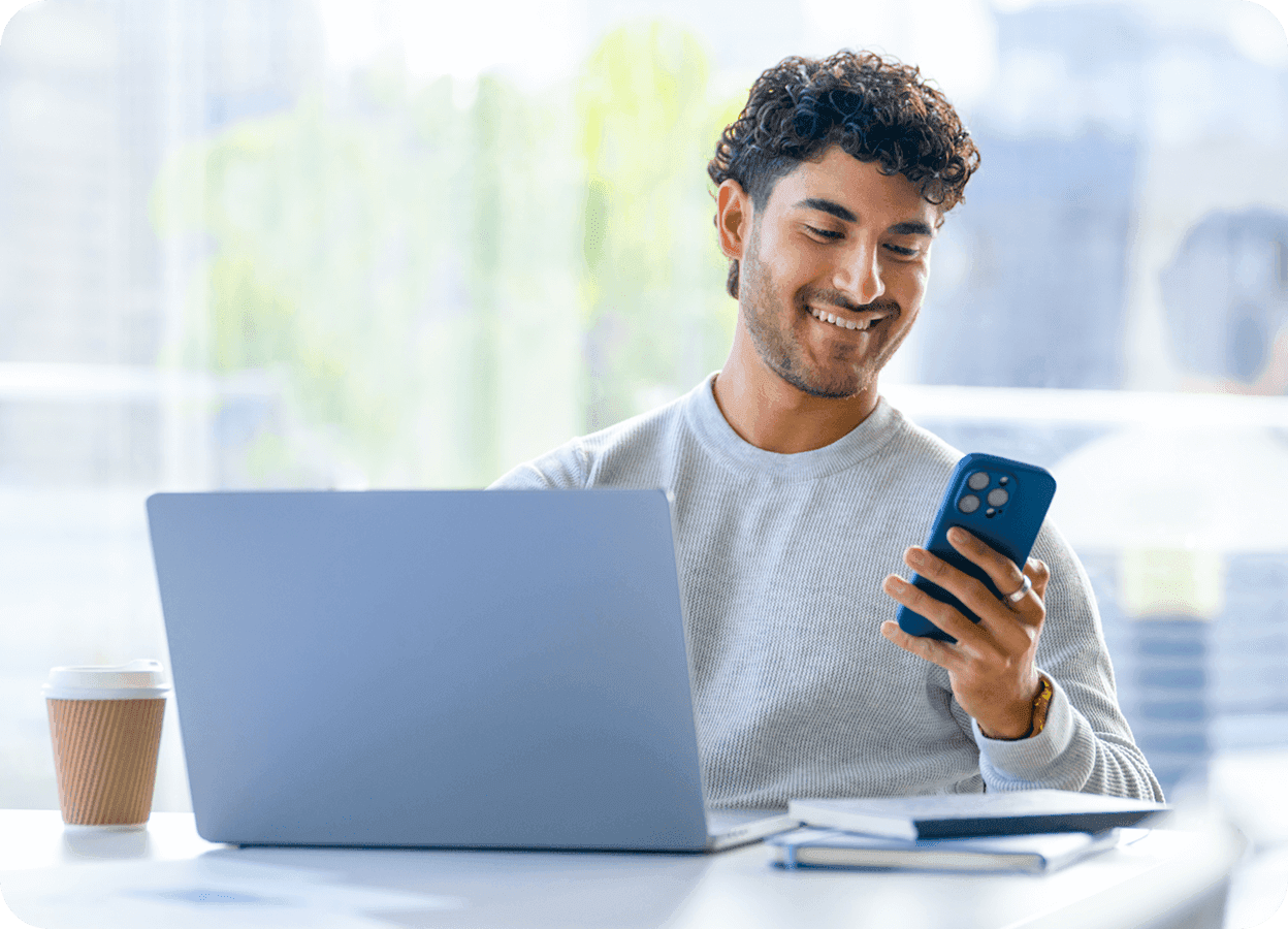 a man is smiling while looking at his phone in front of a laptop