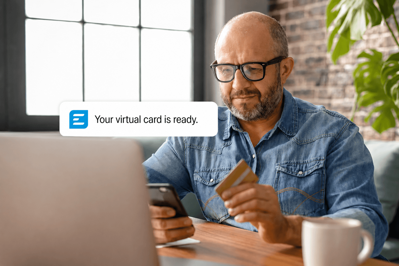 A man in glasses holds a physical credit card while looking at his phone, which displays a "Your virtual card is ready" notification.