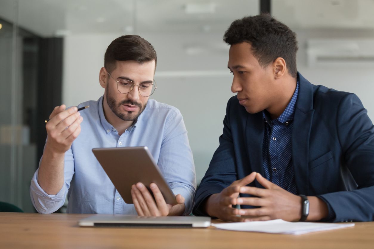 Two professional men discussing content on a tablet in an office.